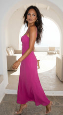 Woman in a pink dress standing in a sunlit room with arched doorways.
