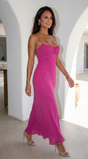 Woman in a pink dress standing in a bright, sunlit room with white walls.